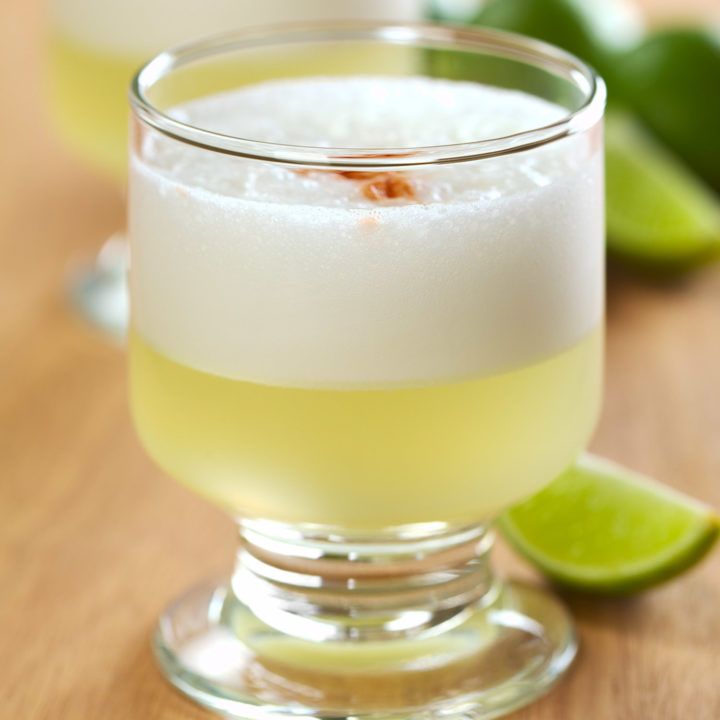 Peruvian cocktail called Pisco Sour made of Pisco (Peruvian grape schnaps) lime juice syrup and egg white (Selective Focus Focus on the front glass rim)