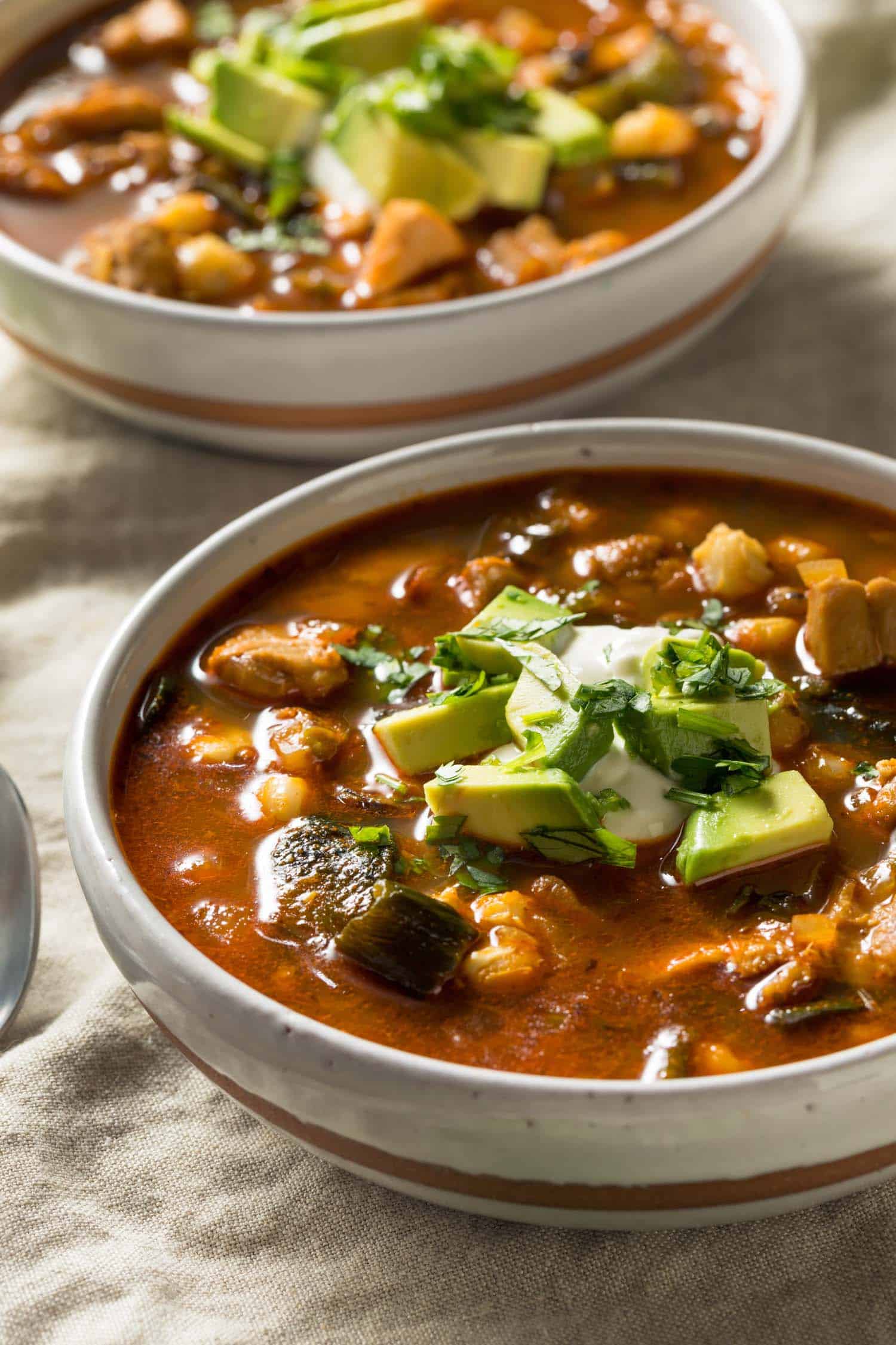 two bowls of Mexican soup called pozole in white bowls garnished with sour cream and avocado