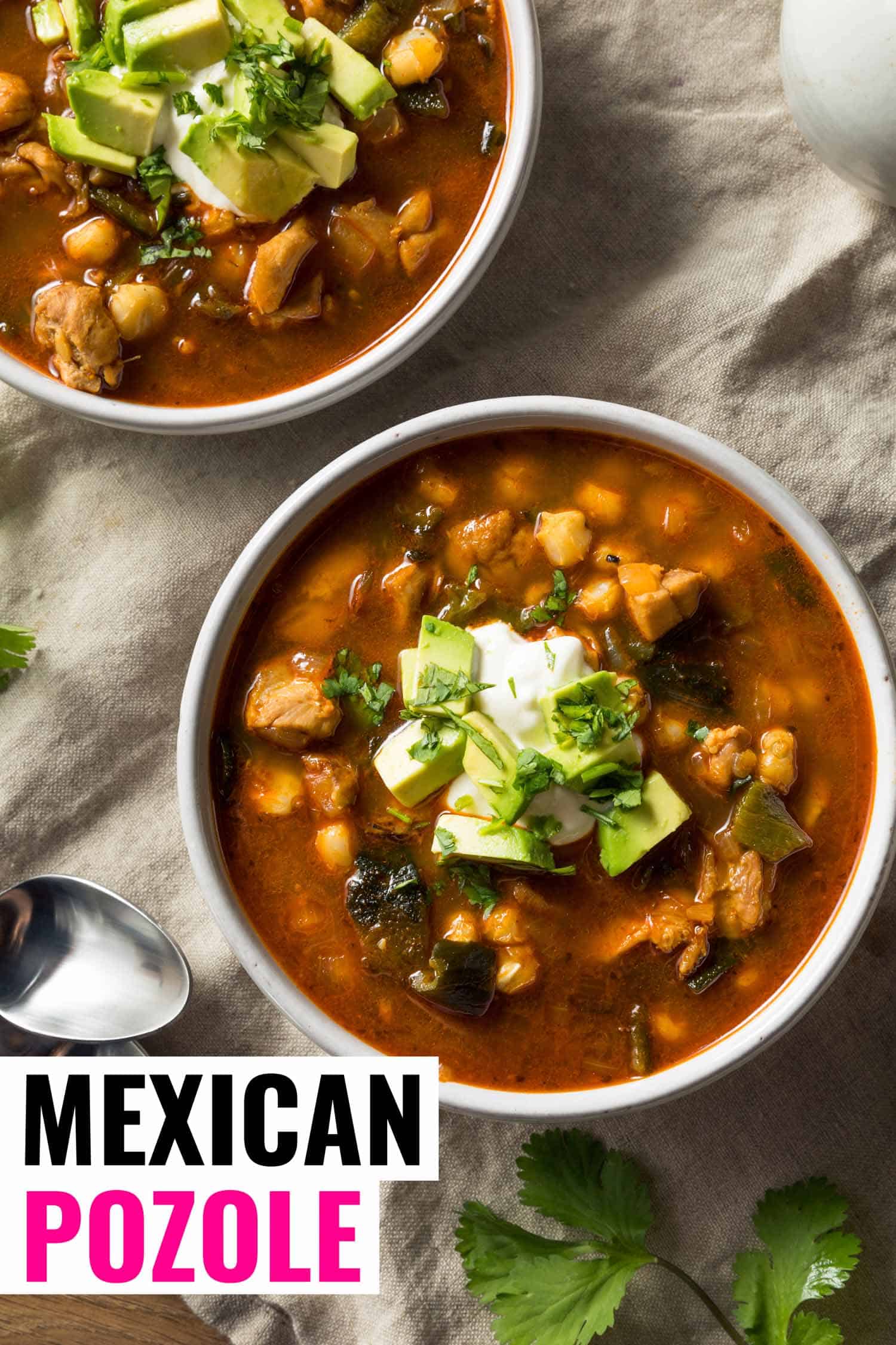 two bowls of Mexican soup called pozole in white bowls garnished with sour cream and avocado