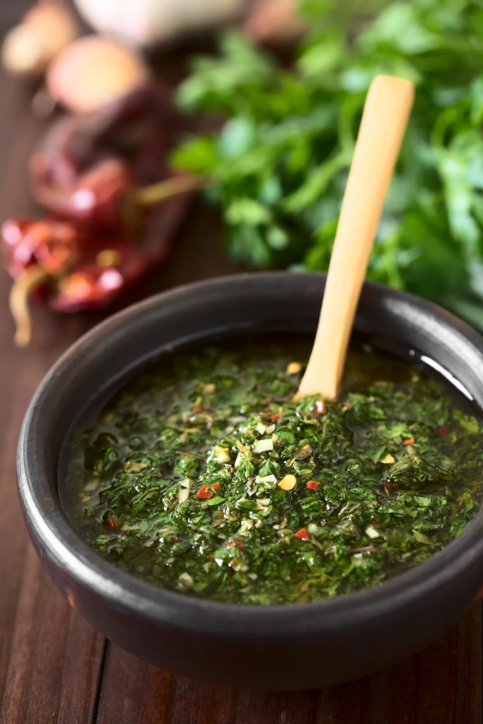 Raw homemade Argentinian green Chimichurri or Chimmichurri salsa or sauce made of parsley, garlic, oregano, hot pepper, olive oil, vinegar, served in rustic bowl, photographed with natural light (Selective Focus, Focus one third into the image)