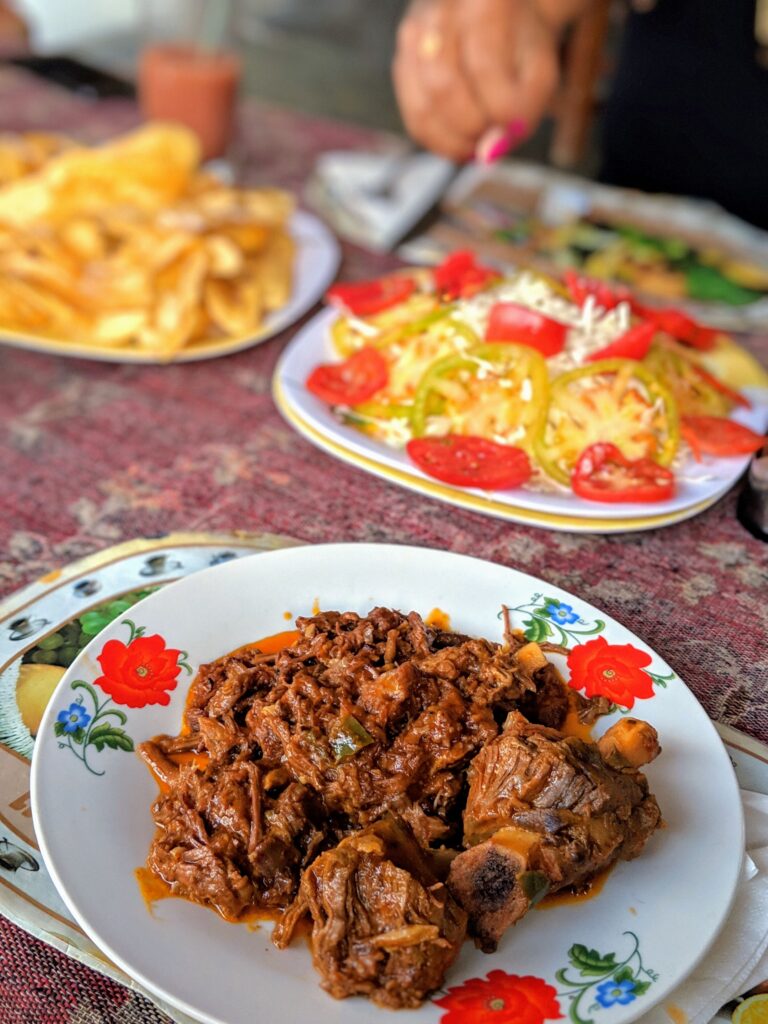 Goat chilindron served in focus on a table with traditional Cuba food in background