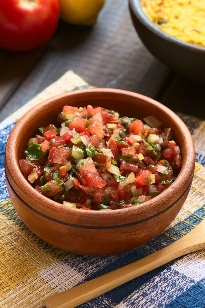 Traditional pico de gallo or Chilean Pebre sauce made of tomato onion aji verde (small green hot pepper) lemon juice and coriander leaves served for barbecue and traditional dishes photographed on wood with natural light (Selective Focus Focus in the middle of the pebre)