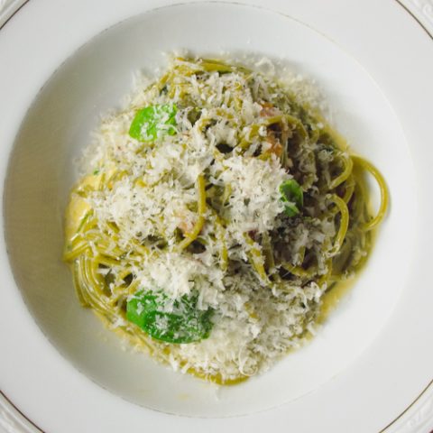 Roasted garlic spaghetti with parmesan, basil and cream on a white plate.