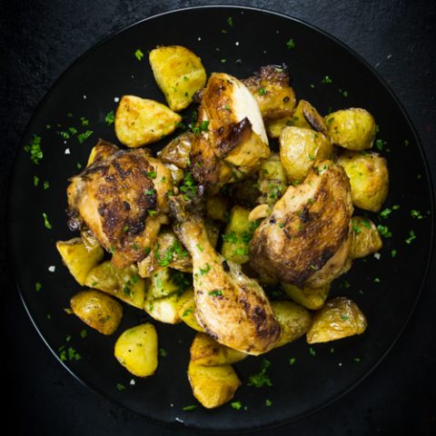 Roasted chicken thighs, drumsticks and potatoes on a black plate