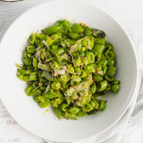 Spicy sugar snap peas in a white bowl on a white table.