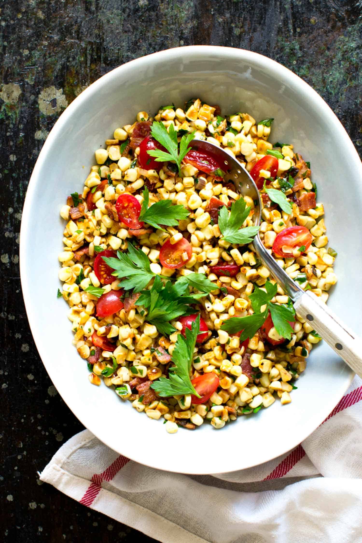 Warm corn salad with ramps in white bowl on black background.