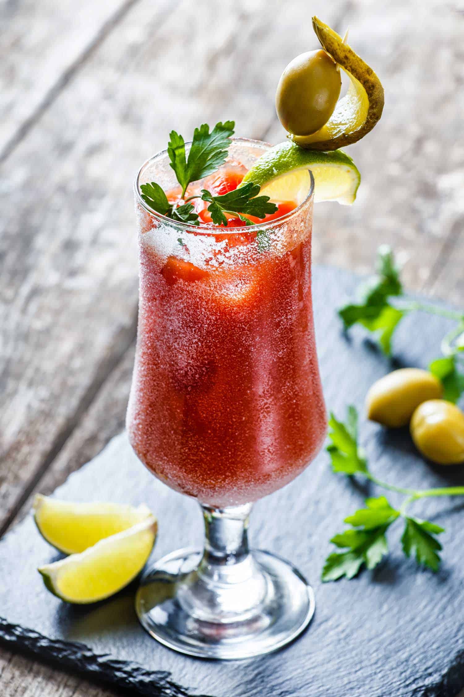 Canadian Caesar cocktails with tomato juice and spicy vodka decorated with pickle and olive garnish on stone slate background on rustic table. Summer drinks and alcoholic cocktails.