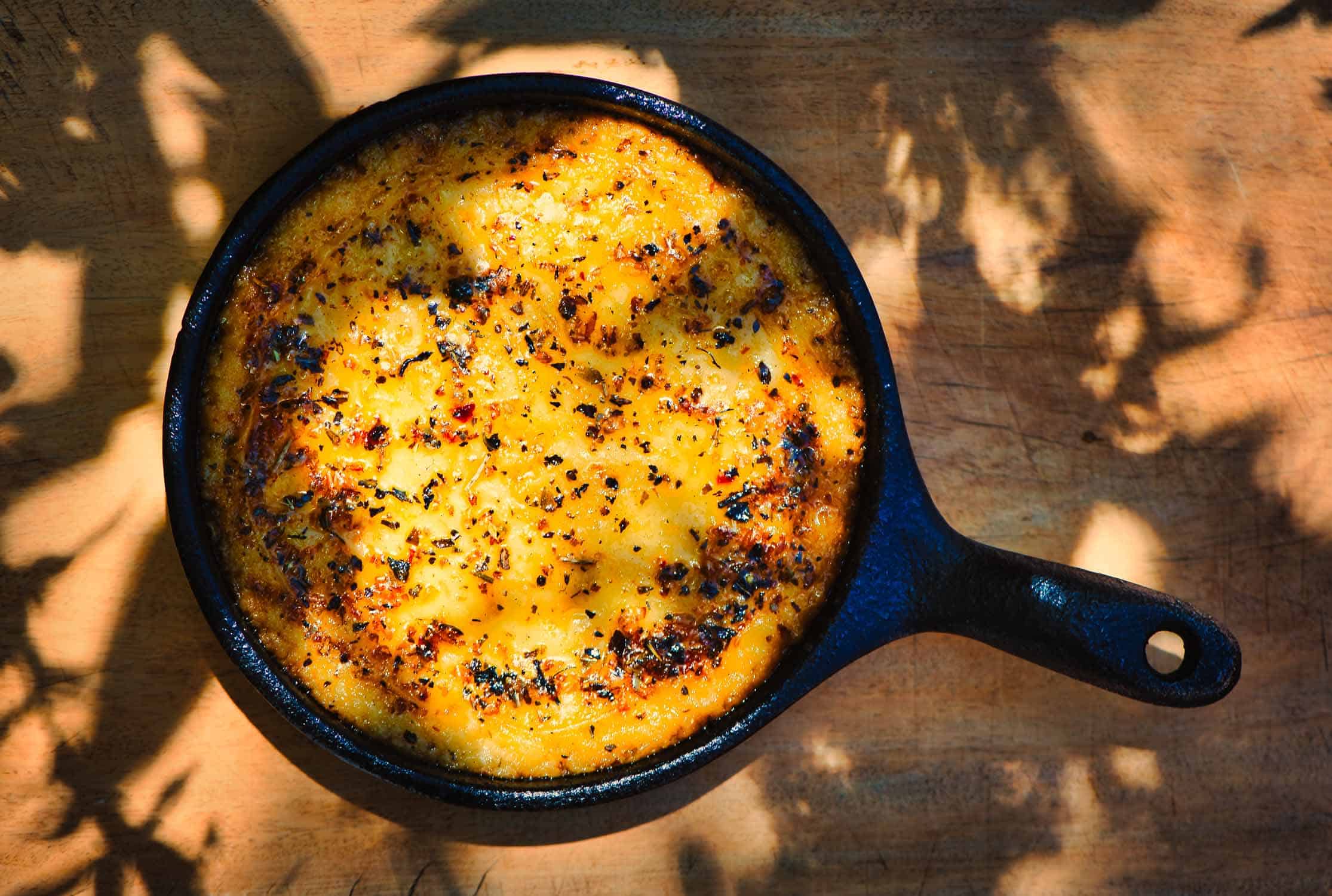 Delicious Argentinian Provolone Yarn Cheese (Provoleta) that was cooked in a cast iron skillet over the embers presented on an old wooden board, province of Buenos Aires, Argentina. Close up scene.