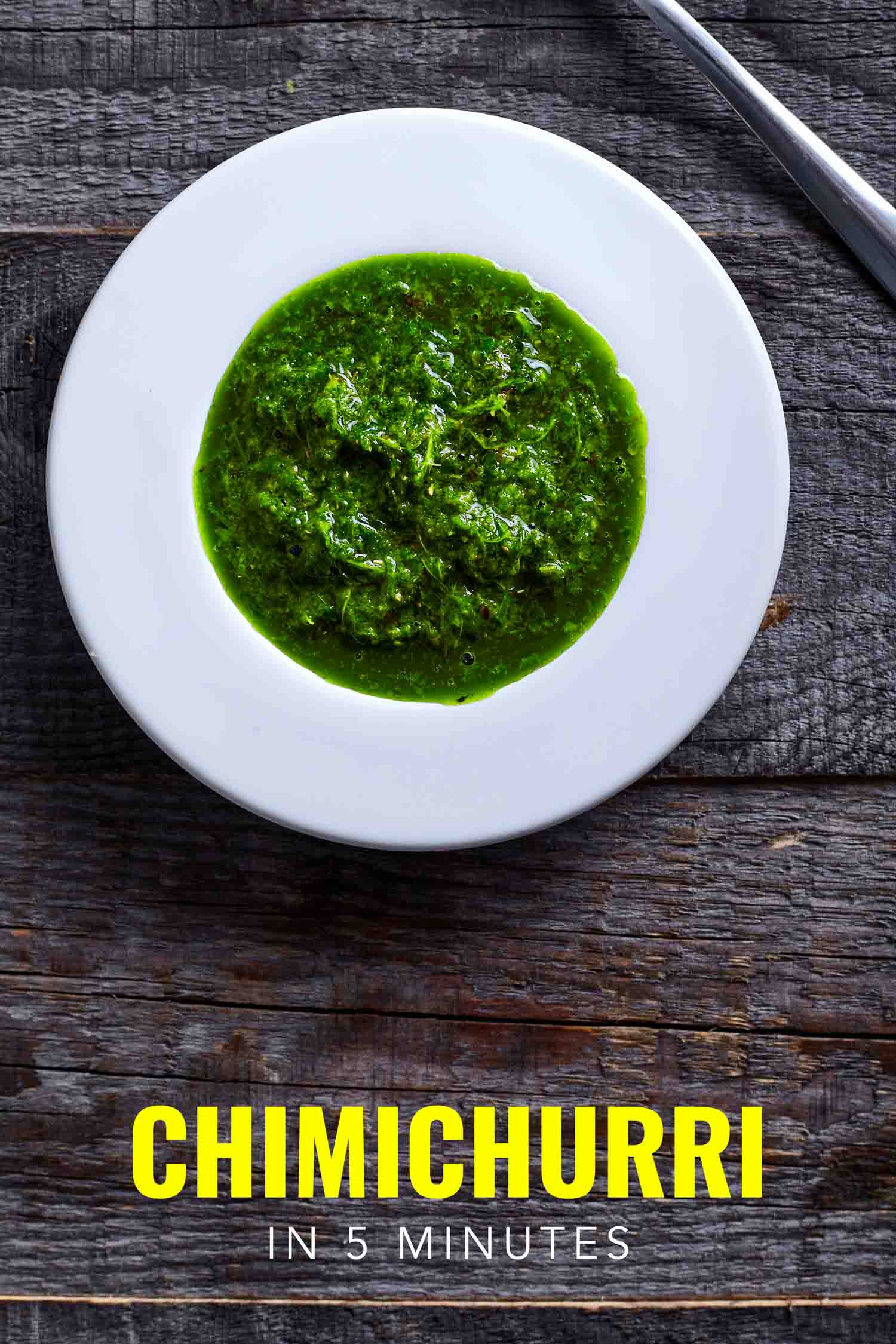 Chimichurri in a white bowl on a wooden background.
