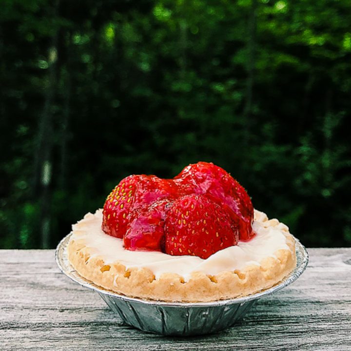Individual strawberry tart on a wooden rail with trees in background.
