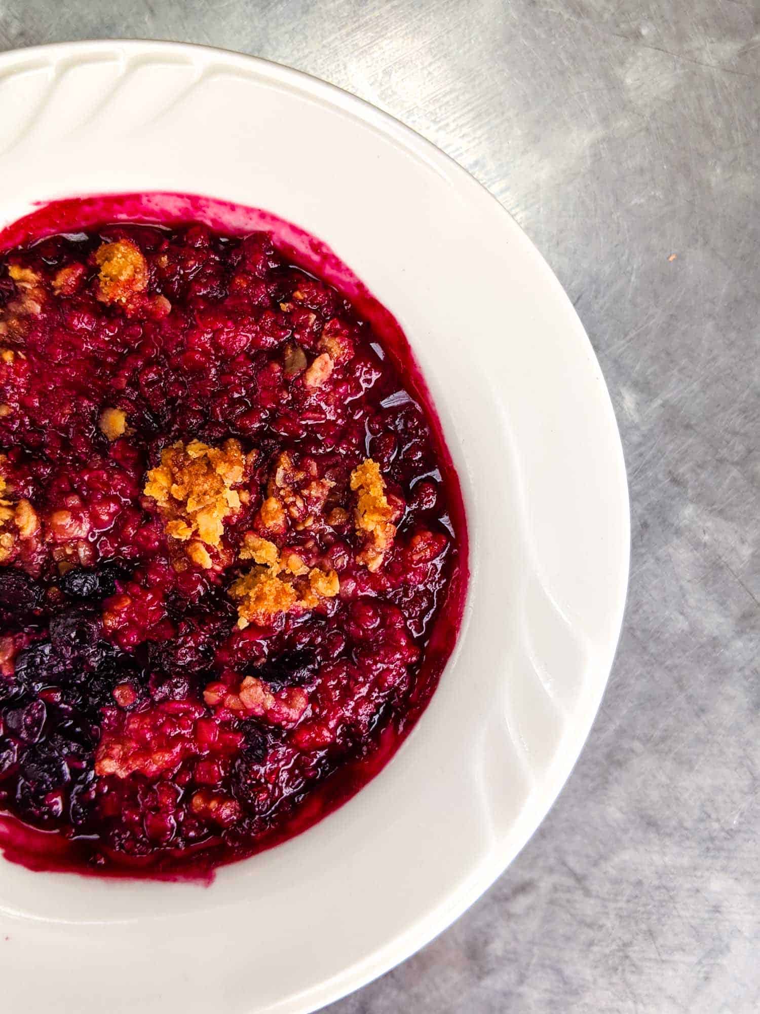 Mixed berry crisp dessert in white bowl on silver background.