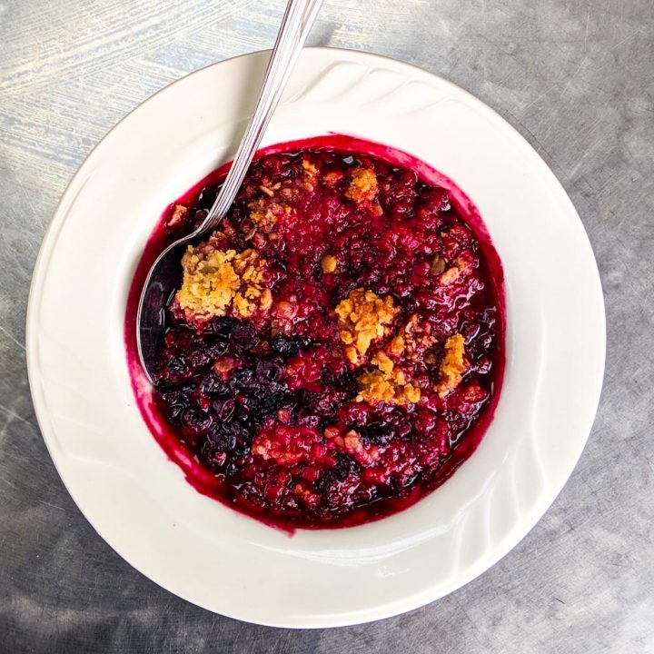 Mixed berry crisp dessert in white bowl on silver background.