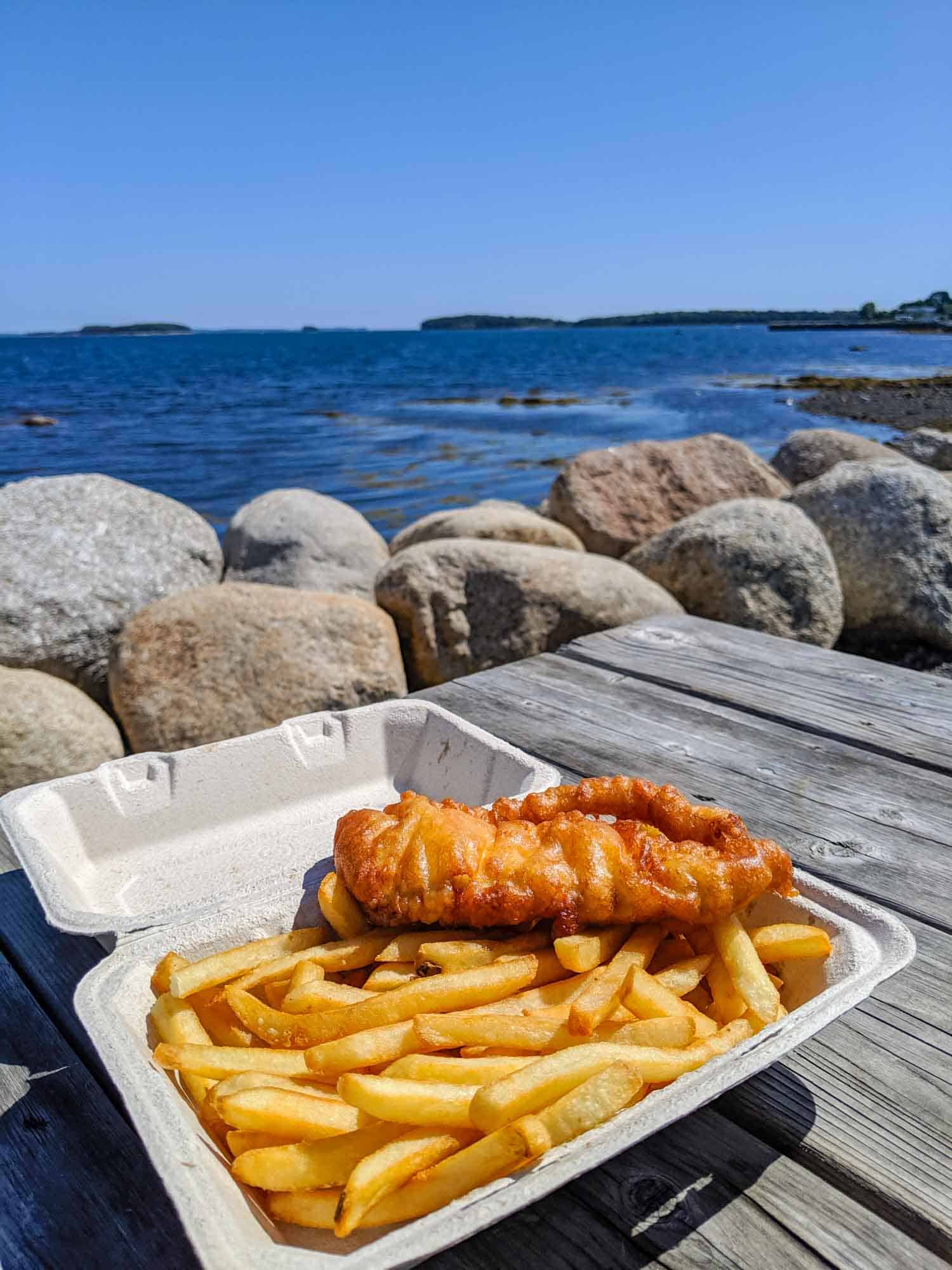 Classic Nova Scotia food, fish and chips on a grey picnic table with view of the ocean