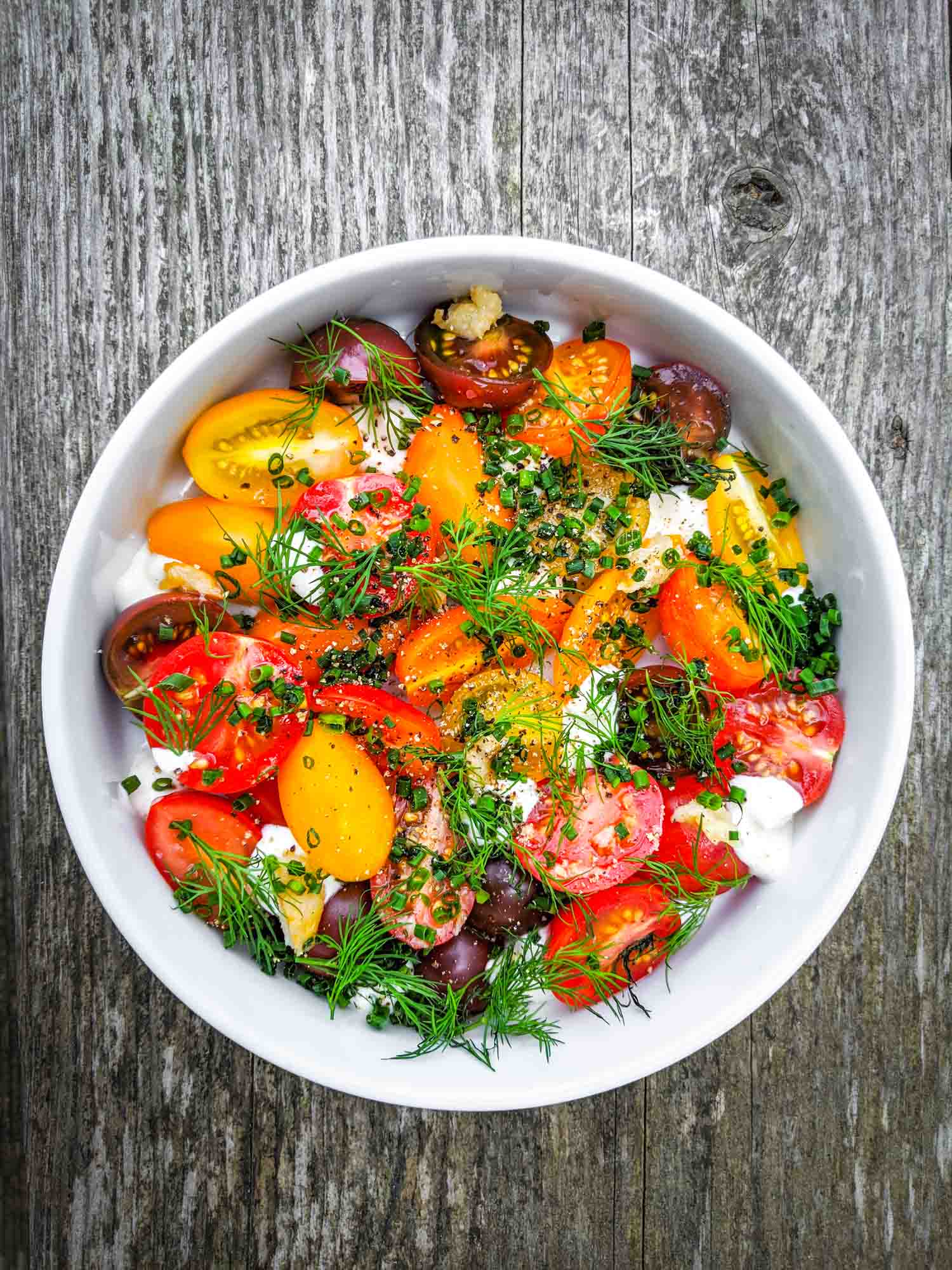 Fresh cherry tomato salad with herbs and creme fraiche in white bowl on grey wood background