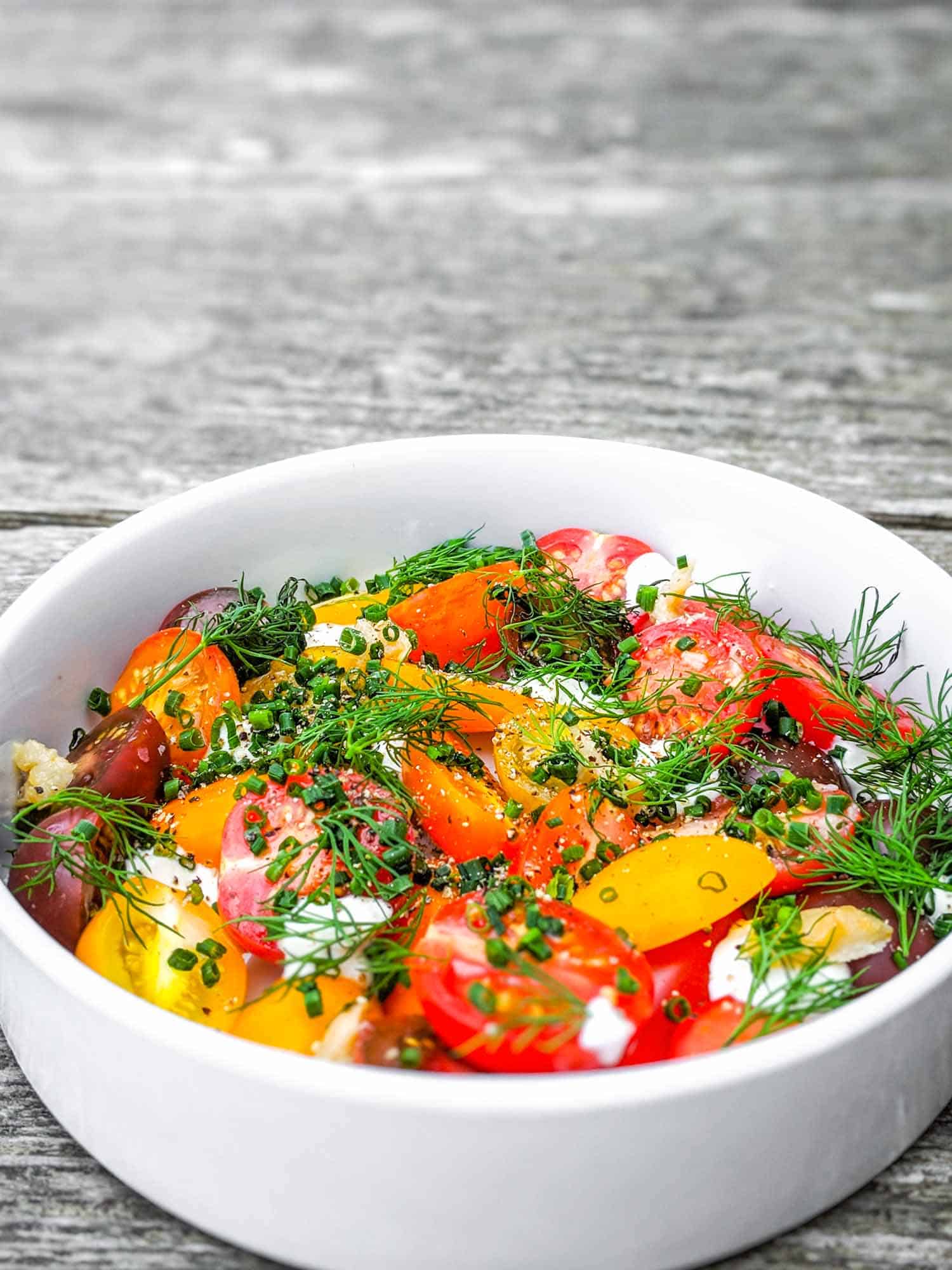 Fresh cherry tomato salad with herbs and creme fraiche in white bowl on grey wood background