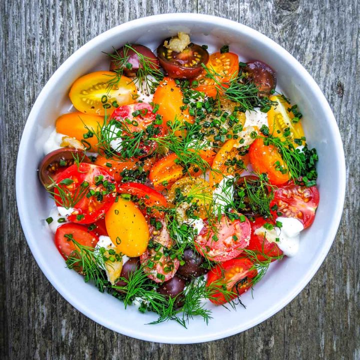 Fresh cherry tomato salad with herbs and creme fraiche in white bowl on grey wood background