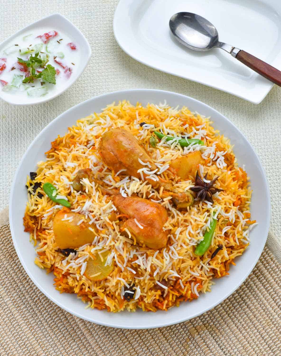 Chicken Biryani. A deliciously colorful rice dish filled with spicy marinated chicken along with salad & raita.