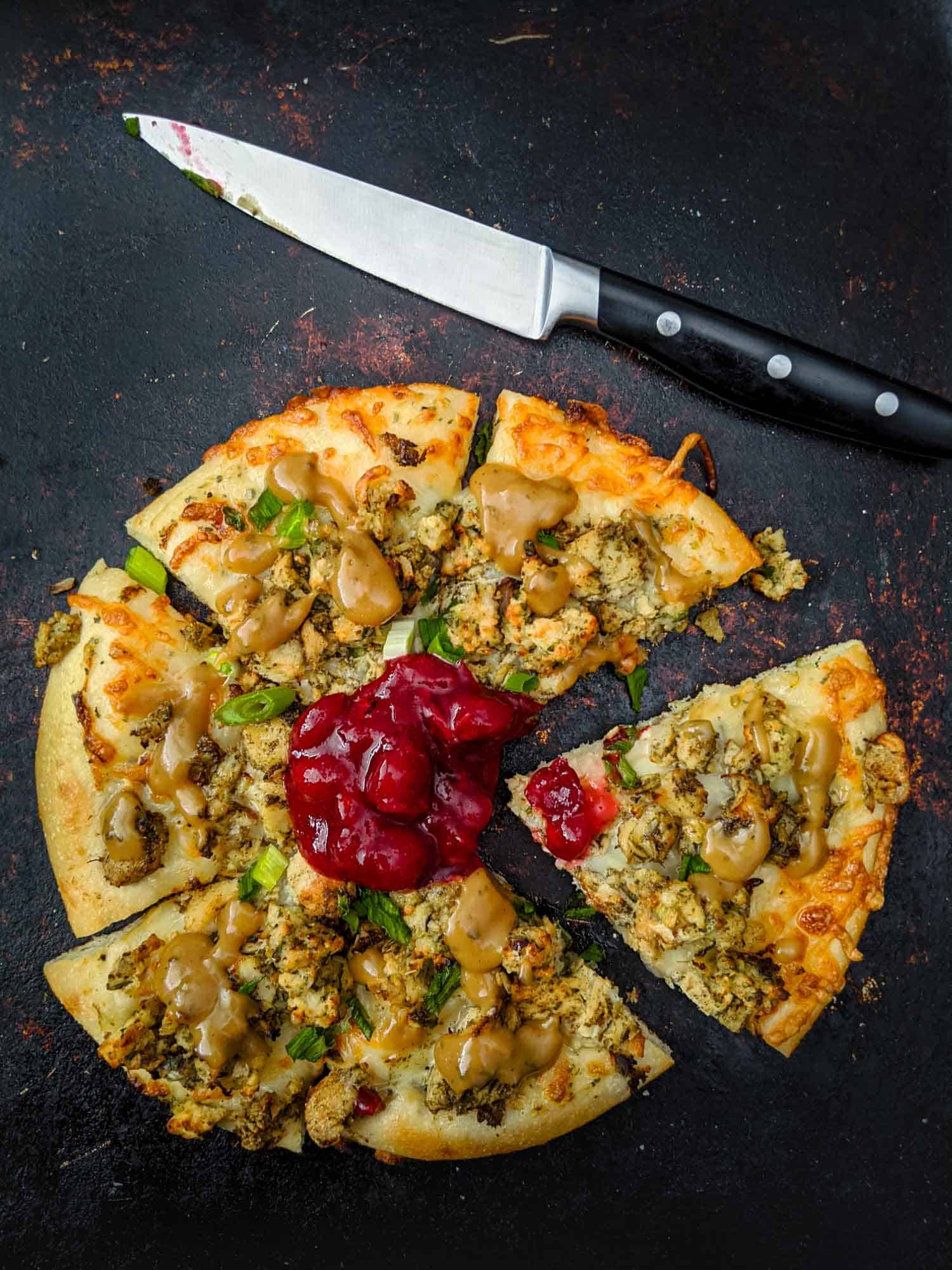 Thanksgiving pizza using turkey dinner leftovers on black.