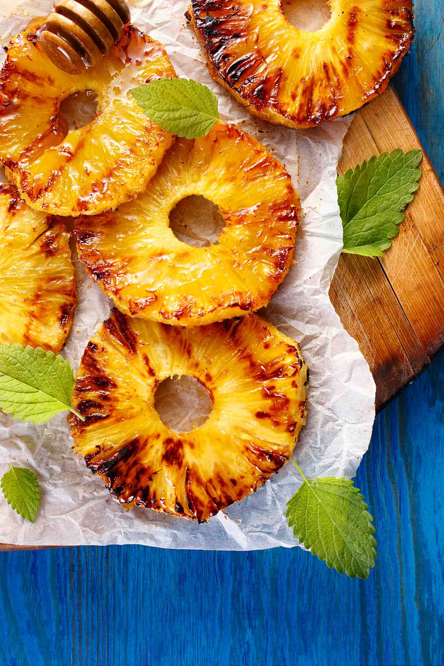 Grilled pineapple slices with addition of honey on a blue table, top view