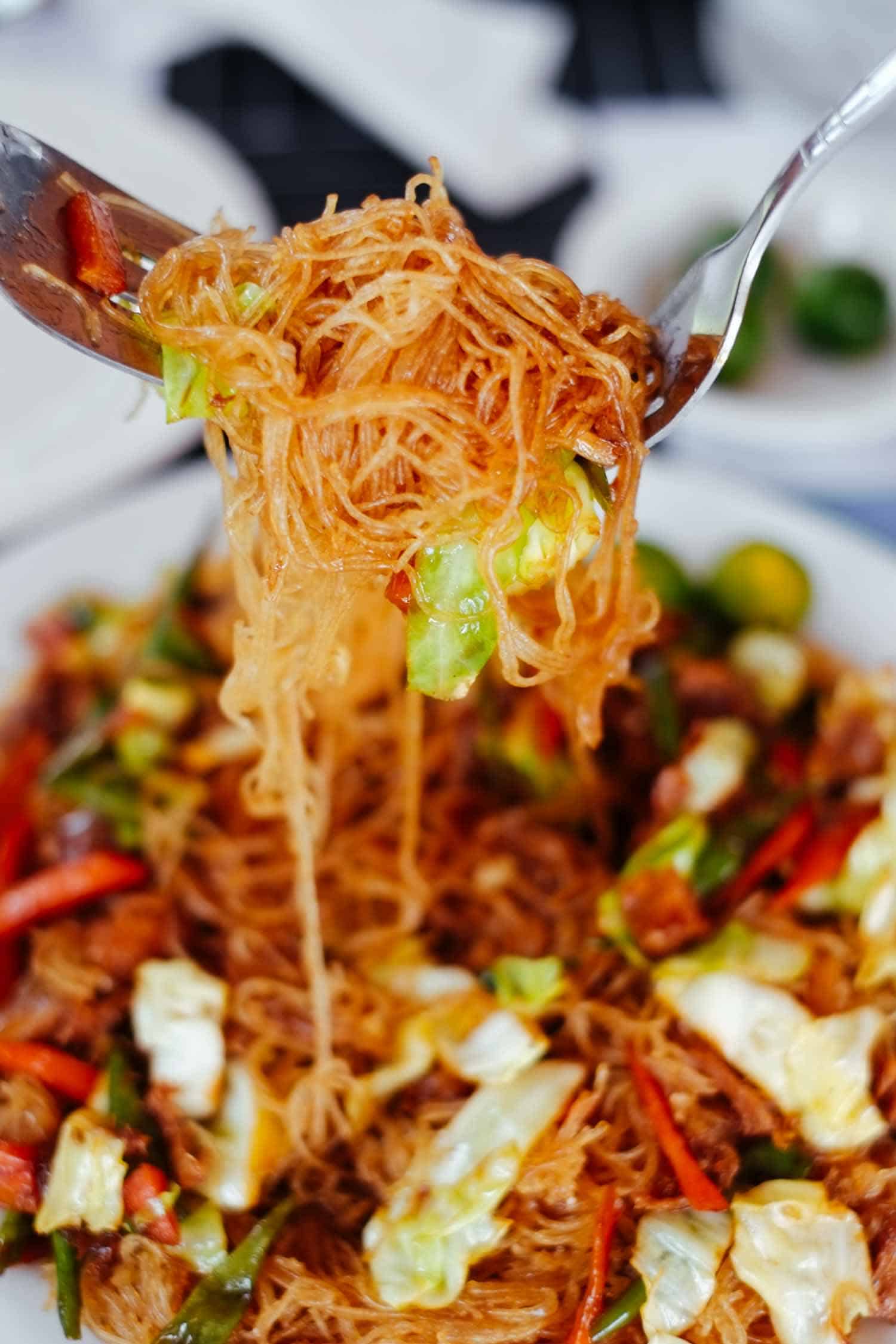 Pancit noodles held on a fork above a Filipino food dish