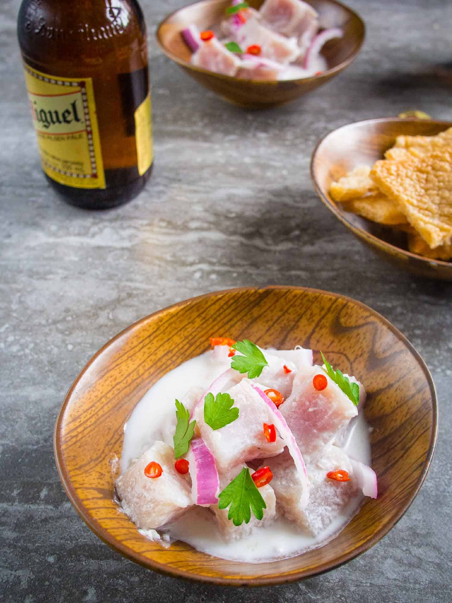 Kinilaw is a common Filipino food similar to ceviche. It is in a pork on a table with beer and chicharron served next to it.
