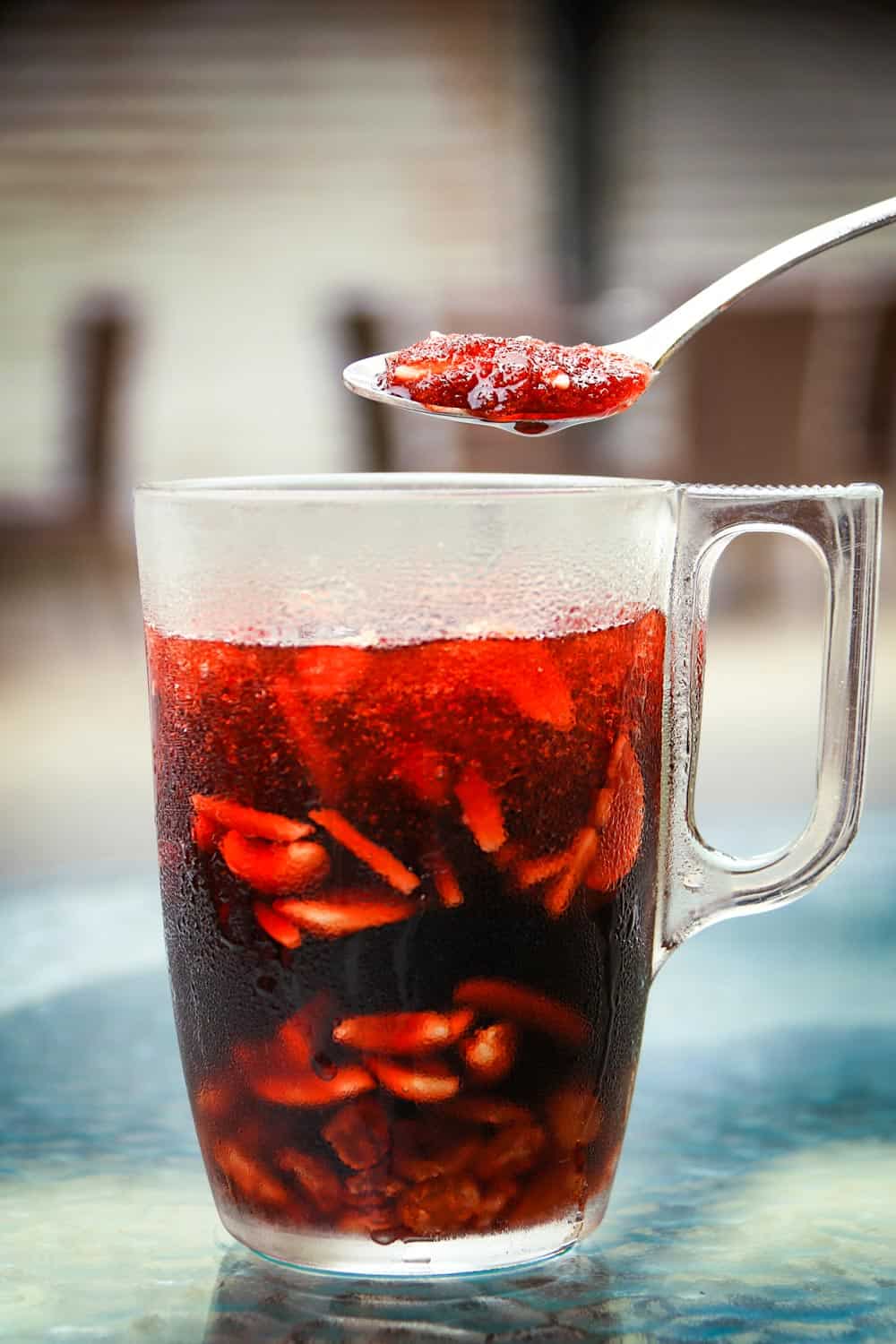 A spoon above a jallab tall glass. Jallab is a refreshing summer drink, popular during Ramadan. It's made of grape, carob molasses, dates, and rose water. It is diluted in water with crushed ice, nuts, and raisins.