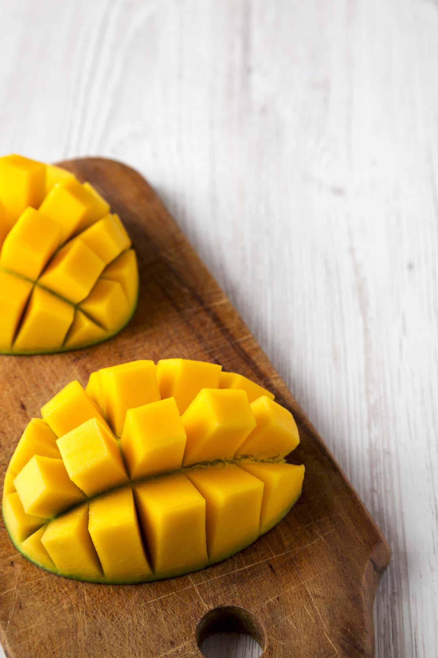 Sweet mango on rustic wooden board on a white wooden table, low angle view. Close-up. Copy space.