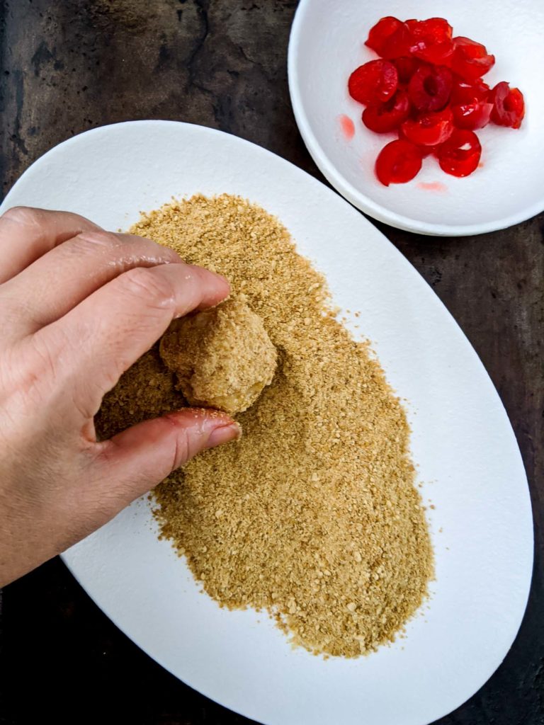 Coconut cherry balls in process shot of rolling in graham cracker crust