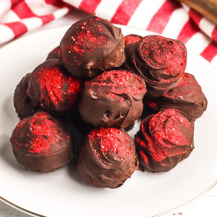 Chocolate strawberry truffles on a white plate with a red and white tea towel.