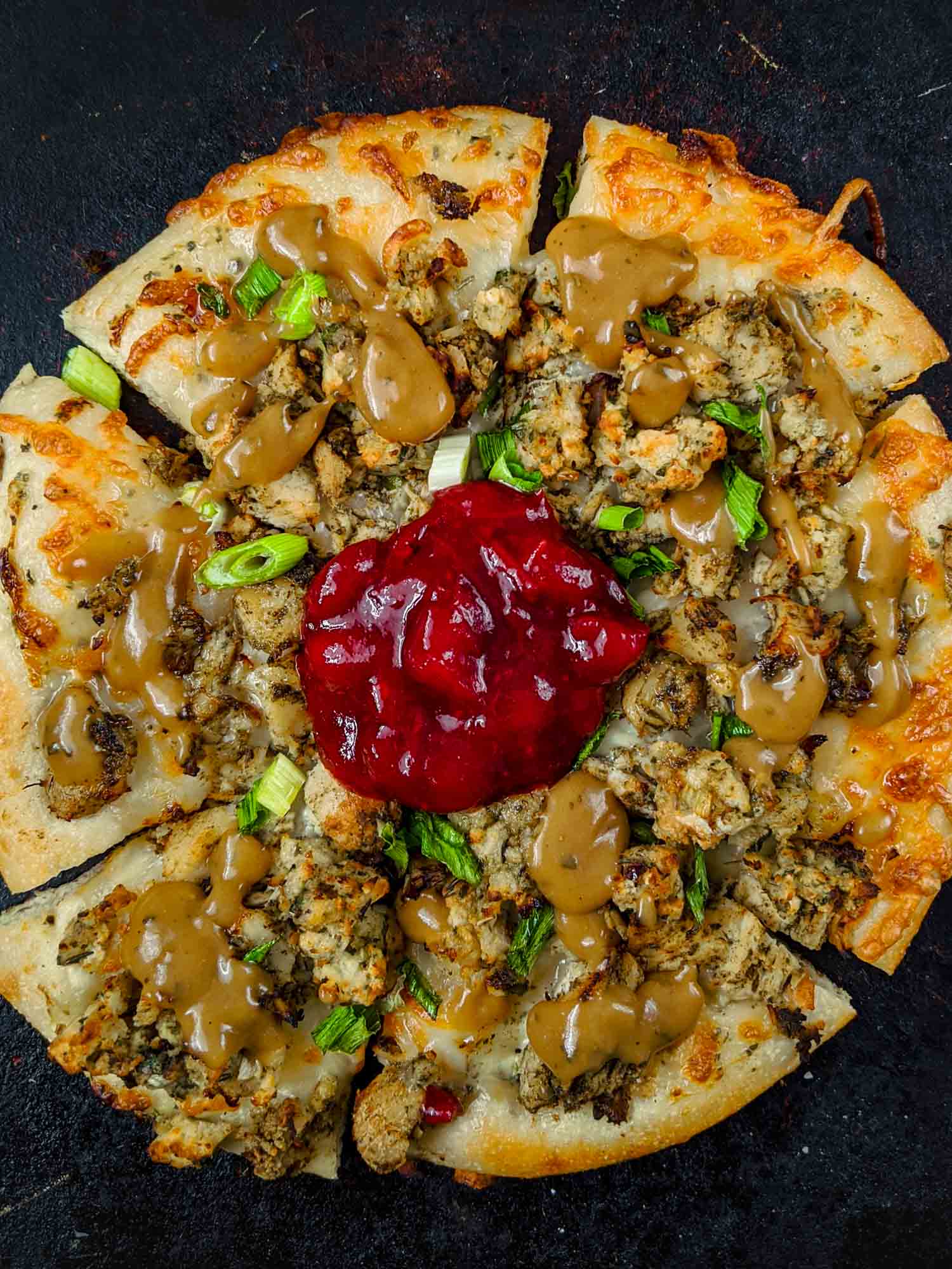 Holiday pizza using turkey dinner leftovers on black.