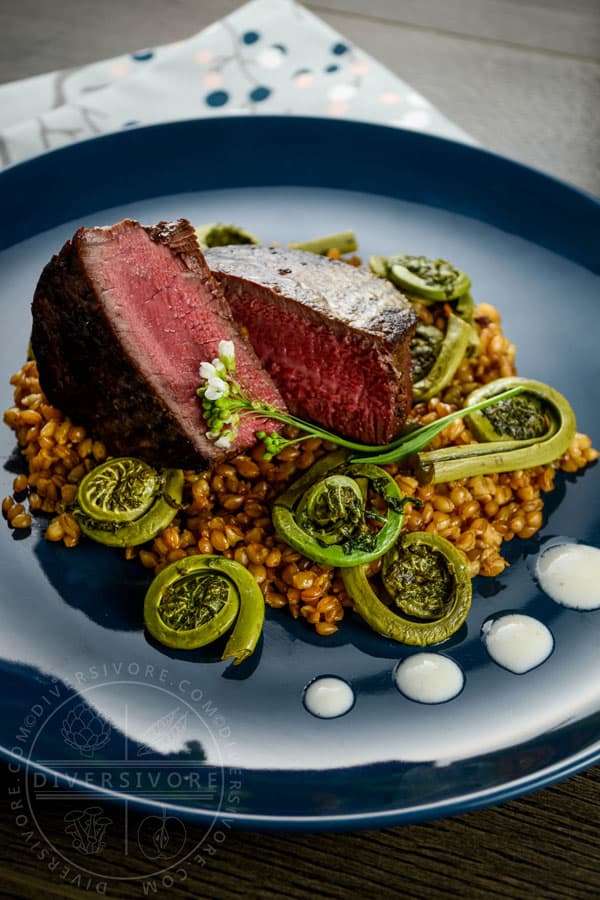 Beef tenderloin with fiddleheads on a blue plate