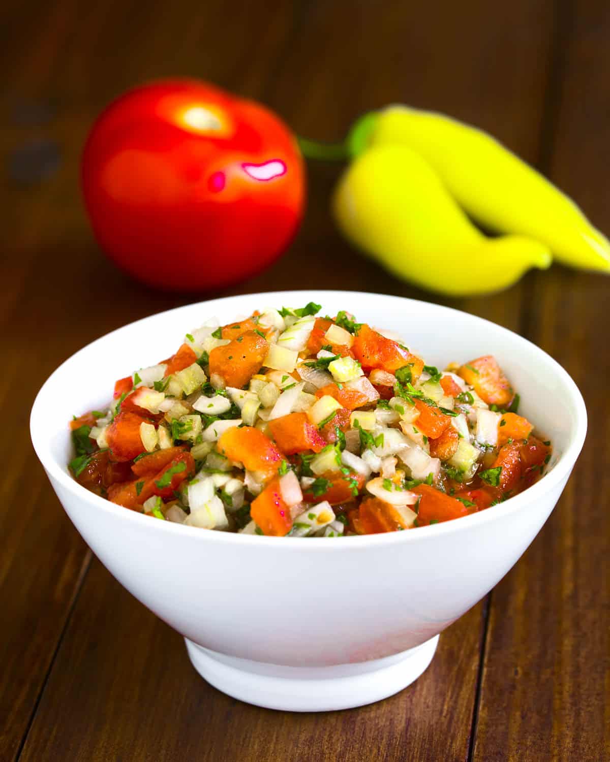 A traditional condiment made of tomato onion garlic spicy aji pepper and coriander photographed on dark wood with natural light (Selective Focus Focus in the middle of the pebre)