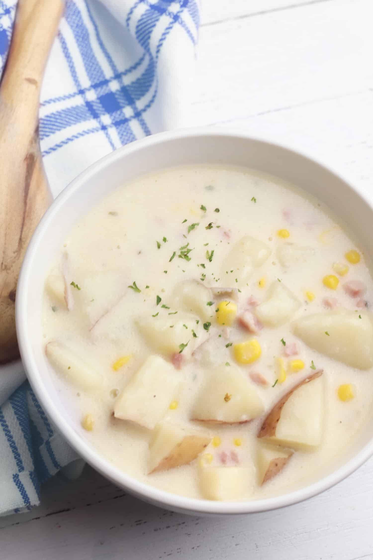 Creamy corn soup in a bowl next to a wooden spoon and tea towel.