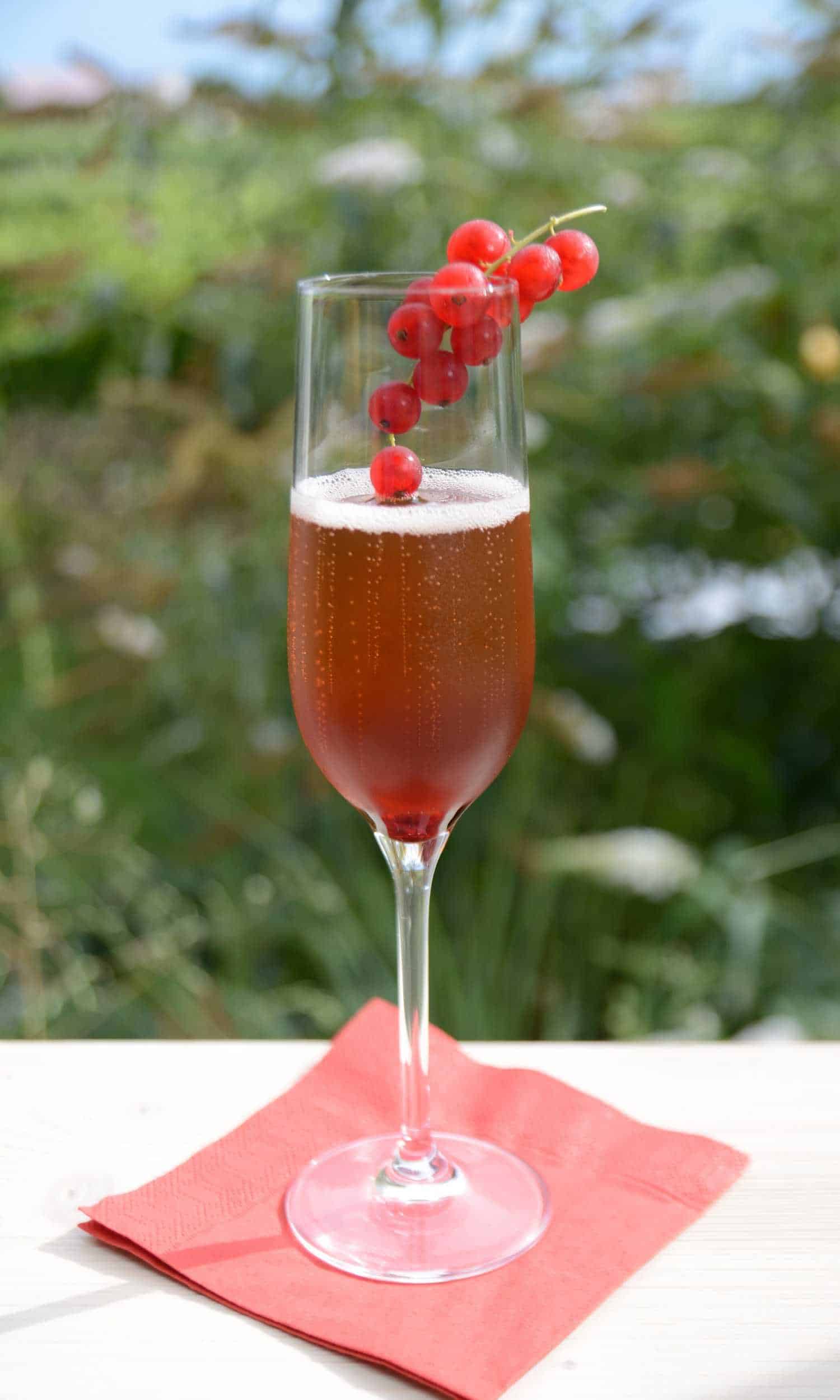 Kir Cocktail in a champagne flute outside on a red napkin.