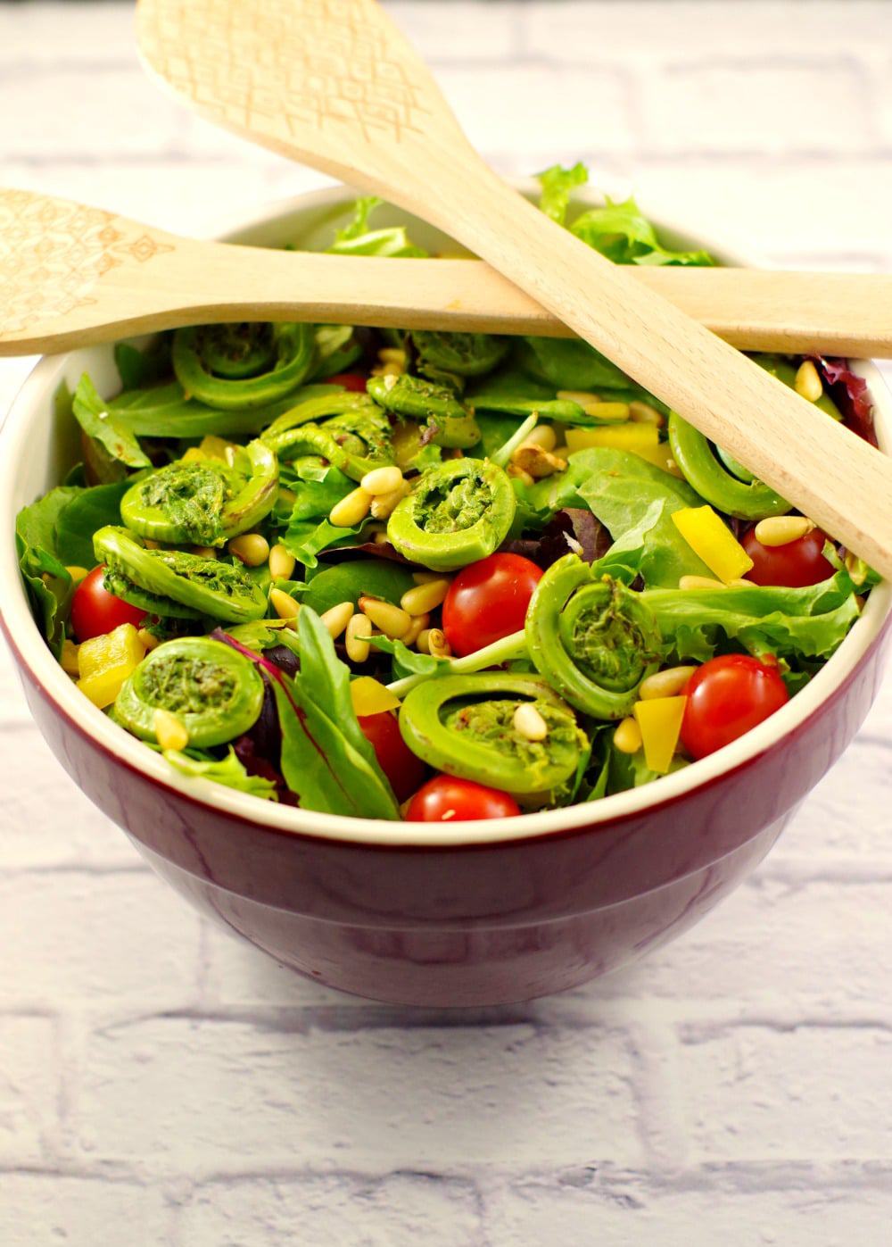 Salad with fiddleheads and blackberry vinaigrette in a large bowl with tongs