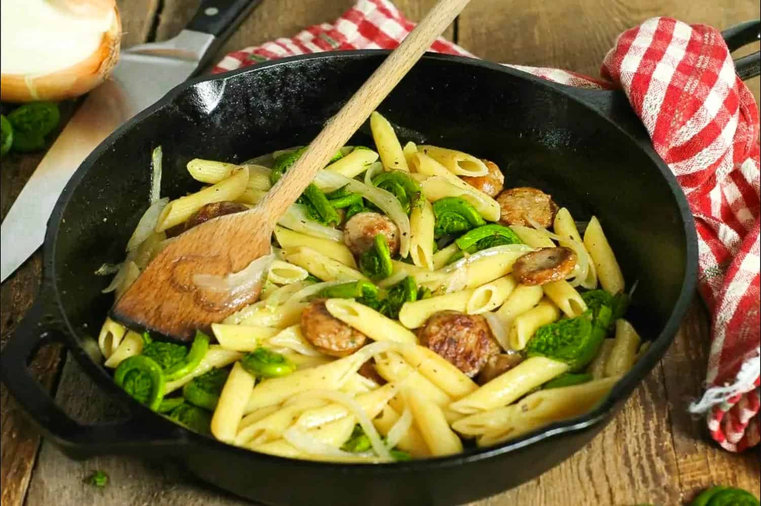 Fiddleheads penne pasta in a cast iron frying pan with a wooden fork