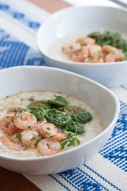 Shrimp and grits with fiddleheads in white bowls on a blue tablecloth