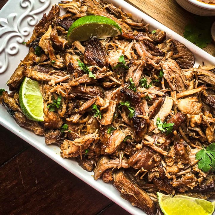 Mexican pork carnitas on a white tray with lime and cilantro