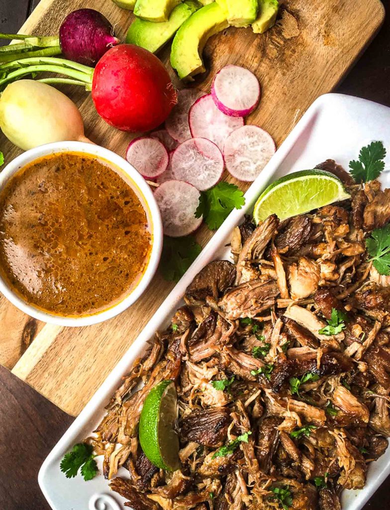 Instant pot pork carnitas on a tray with sauce, radishes and lime