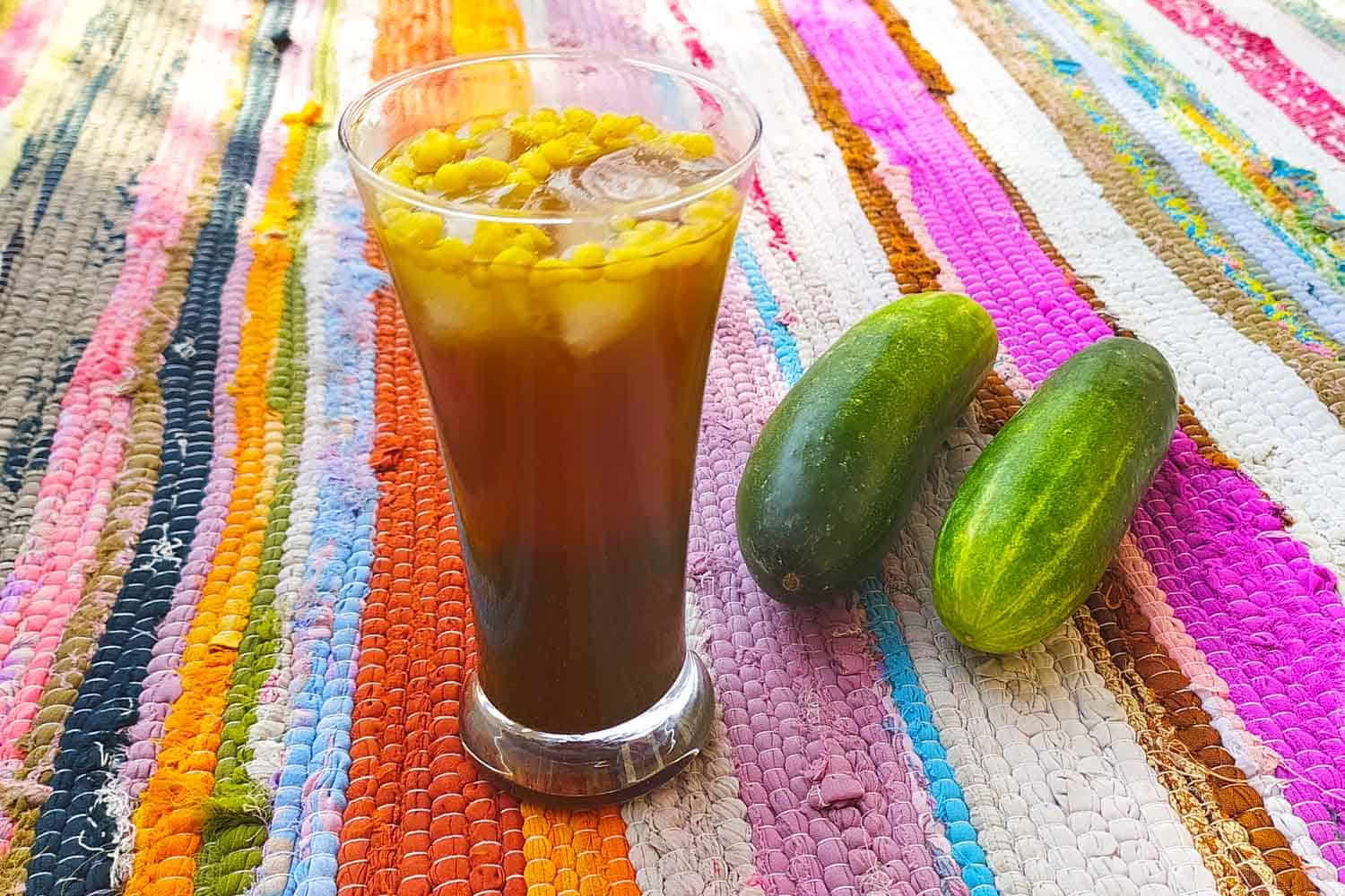 Indian cocktail Jal Jeera Vodka on a colourful rug next to cucumber.