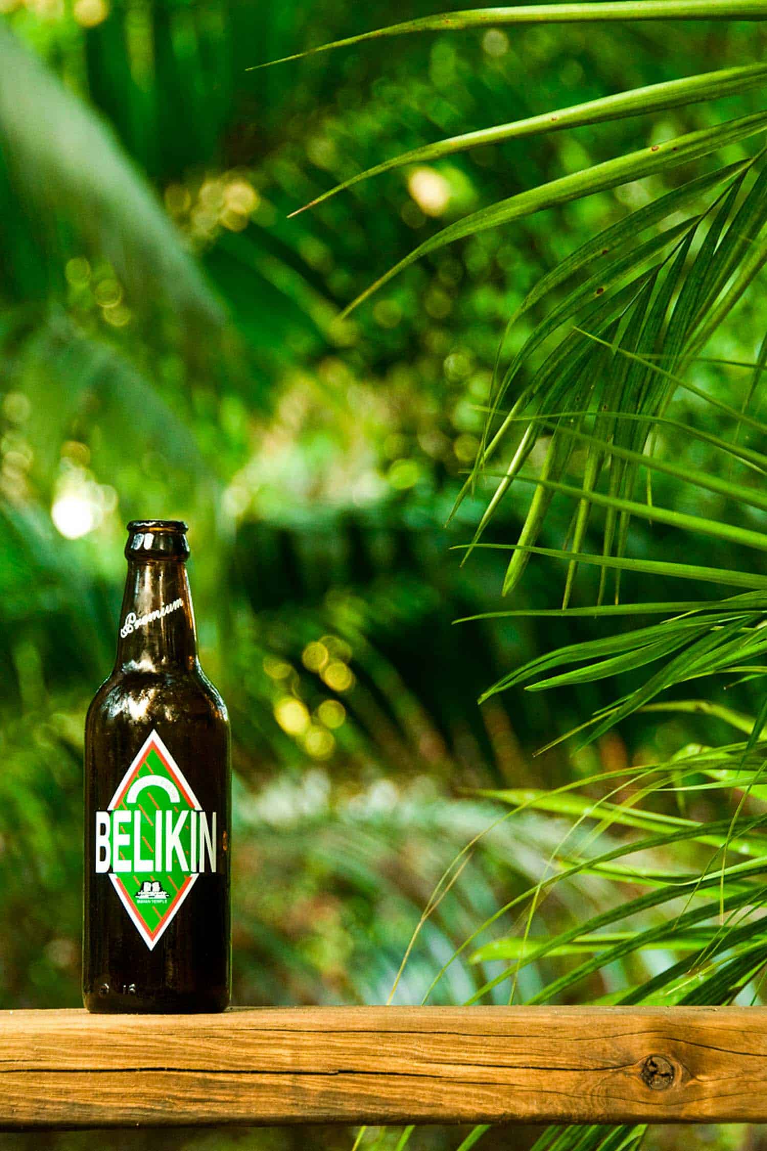 Belizean beer Belikin on a ledge with tropical trees behind it.