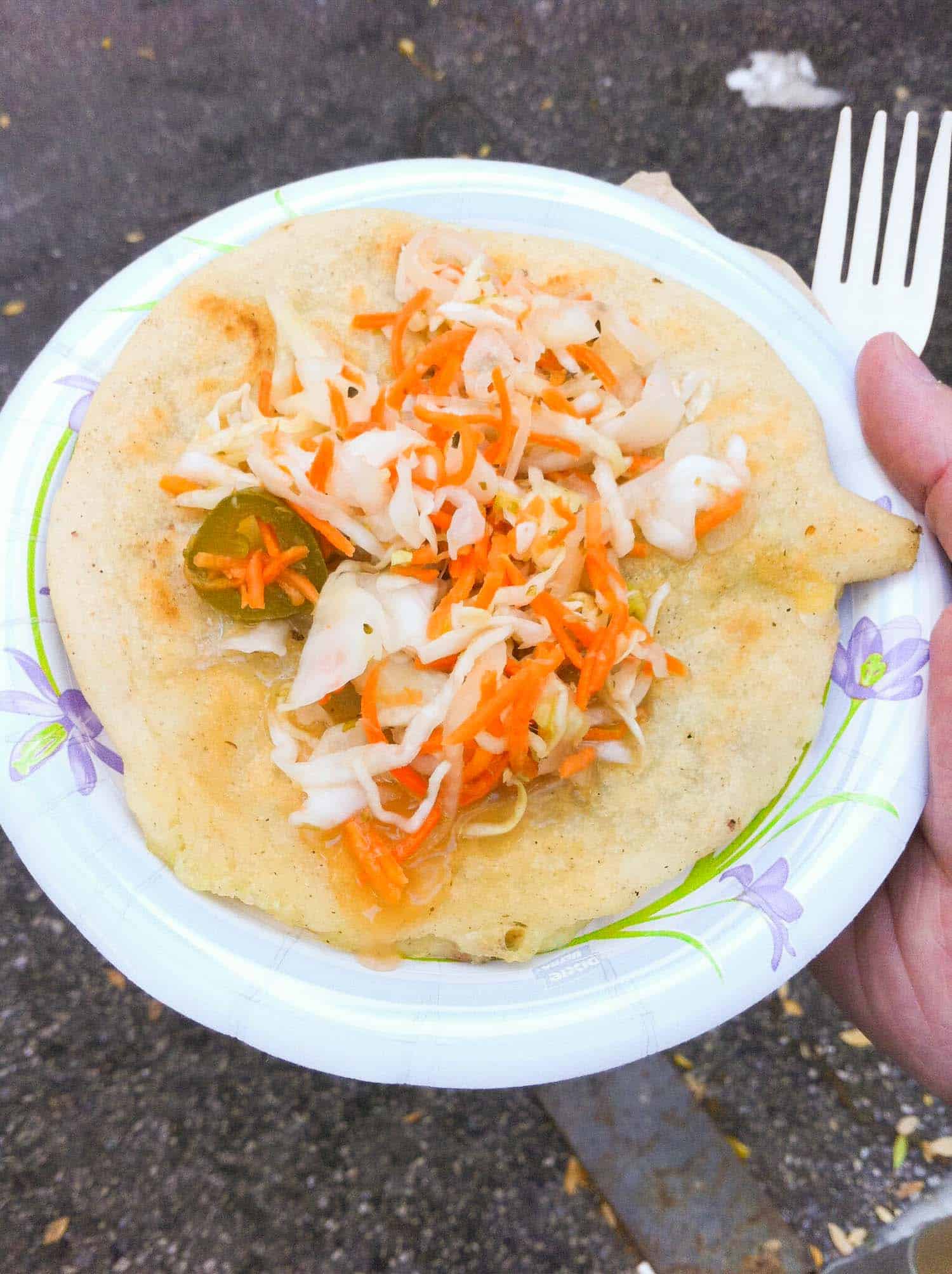 Belizean food pupusa on a paper plate topped with pickled cabbage and carrot