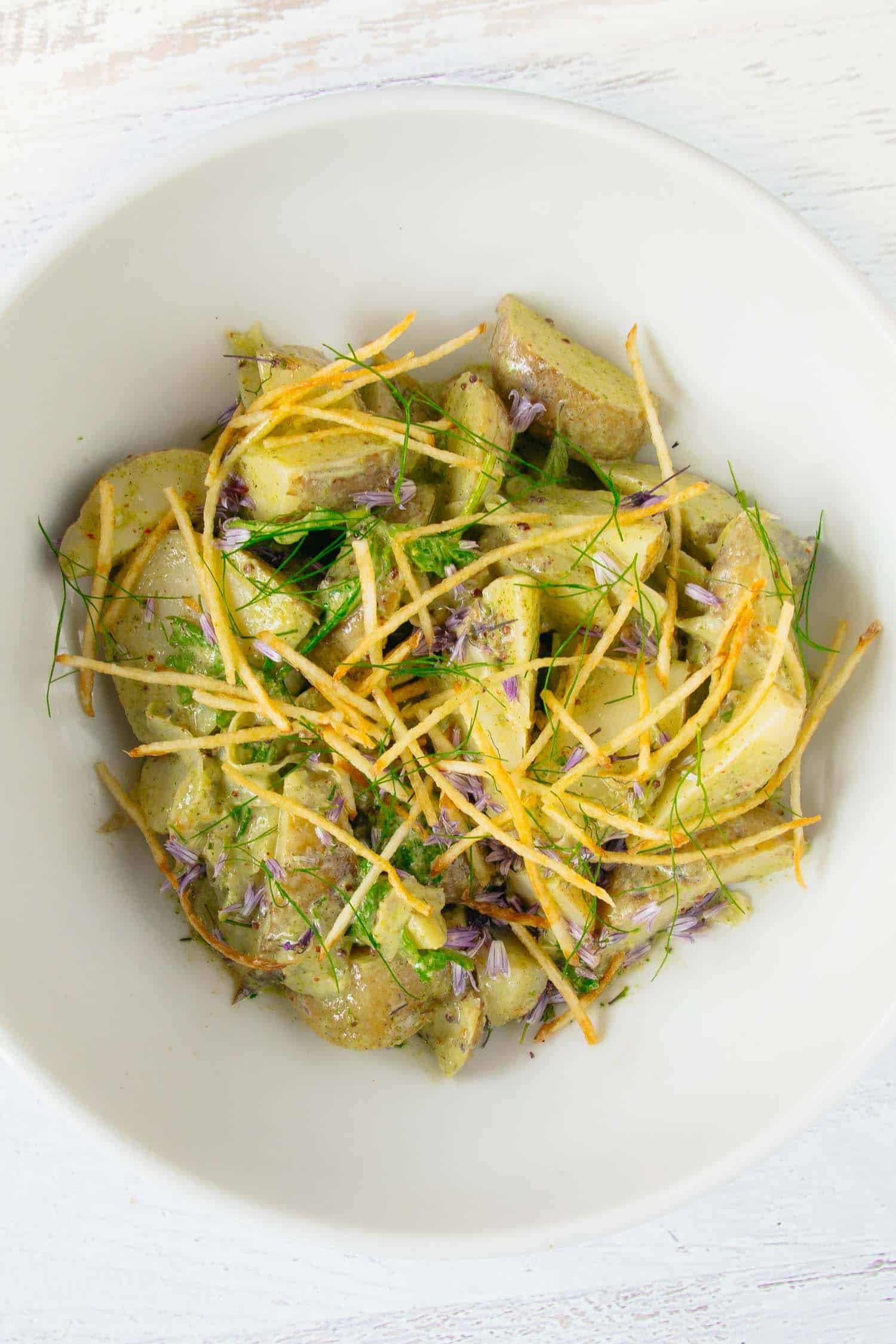 Potato salad with green garlic dressing in a white bowl on a white background