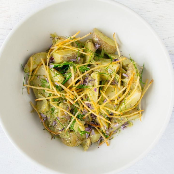 Green garlic potato salad in a white bowl on a white background