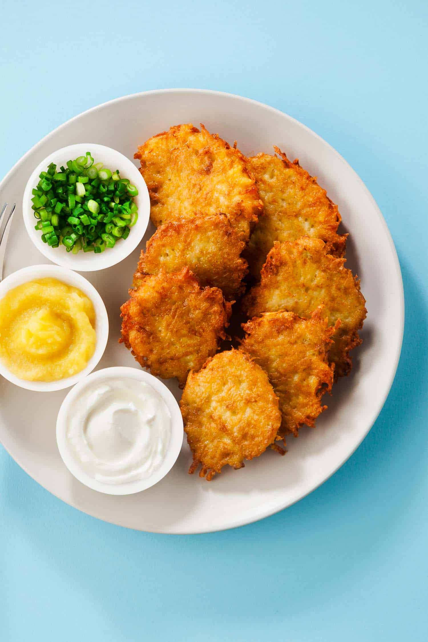 Potato pancakes, latkes or boxty and sauces from sour cream, yogurt, apple sauce and finely chopped green onion isolated on a blue background