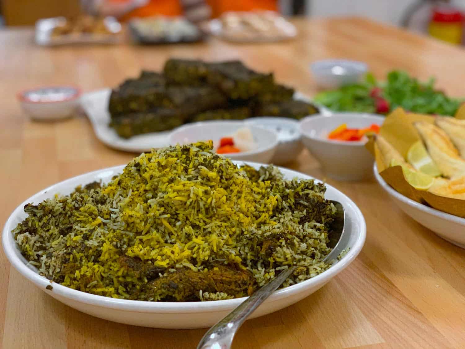 Sabzi polo a traditional Nowruz food rice dish in a white bowl on a table with other food.