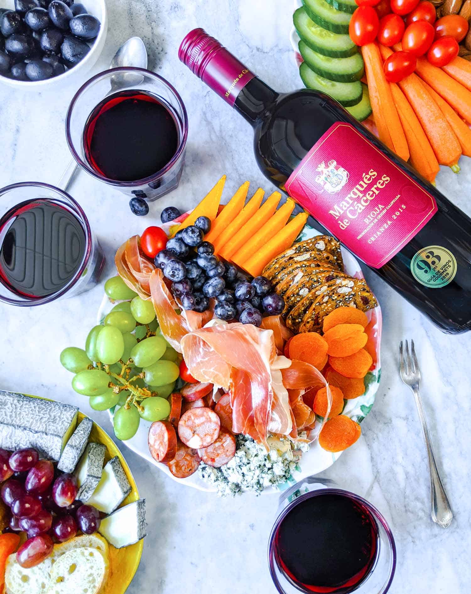 Spanish wine bottle and glasses with table of cured meats, cheese and fruit