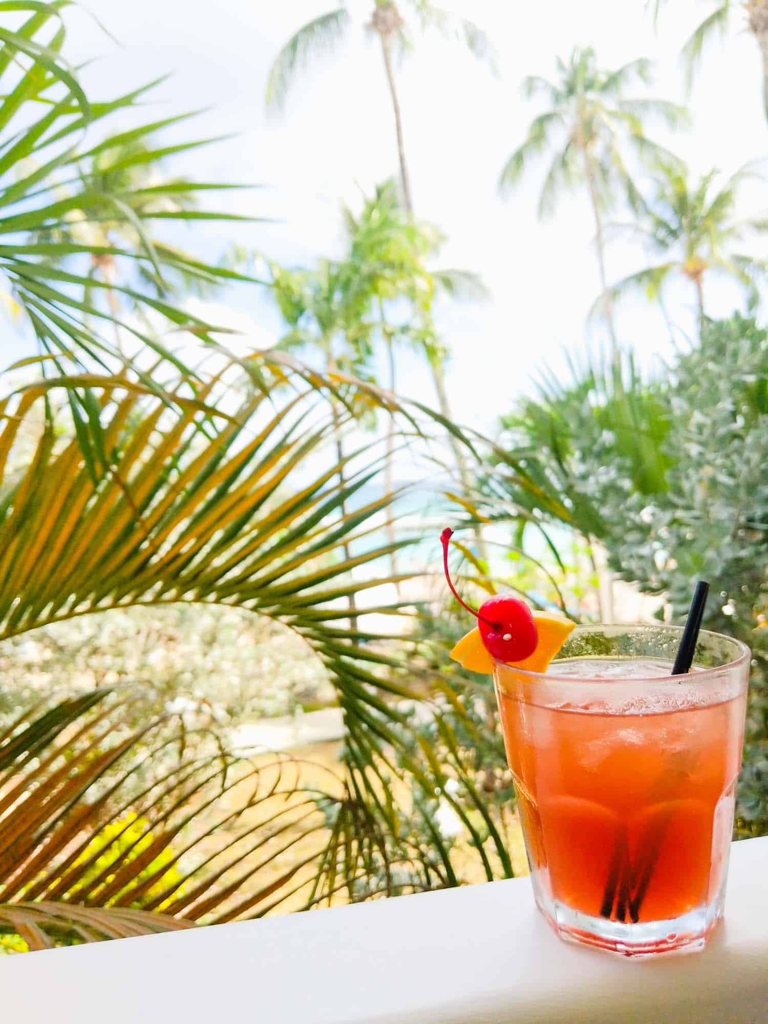 Jamaican rum punch, one of the most popular drinks in Jamaica, on a railing with palm trees in the back.