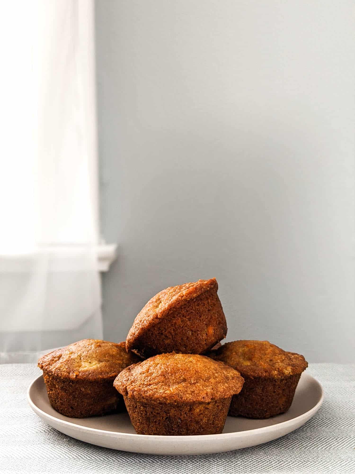 Pineapple carrot muffins on a plate in front of a window.