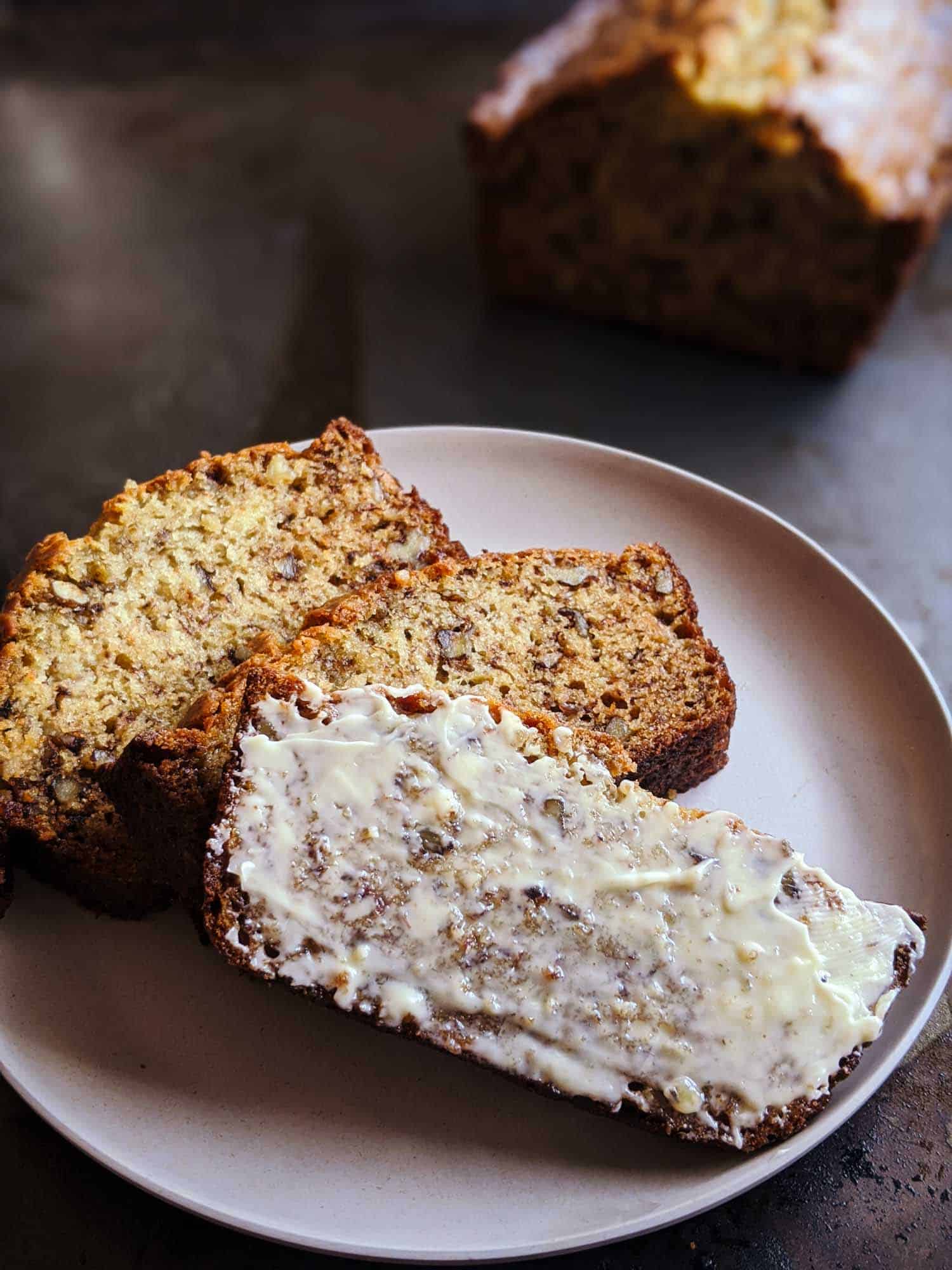 Old fashioned banana bread on a tray, one slice is buttered
